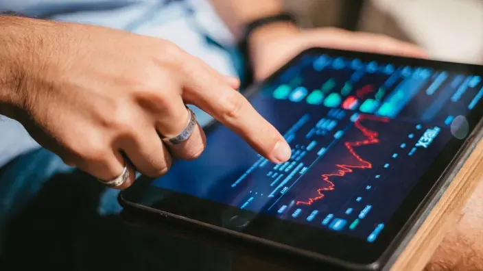 Persona analizando un gráfico de mercado financiero en una tablet con indicadores bursátiles