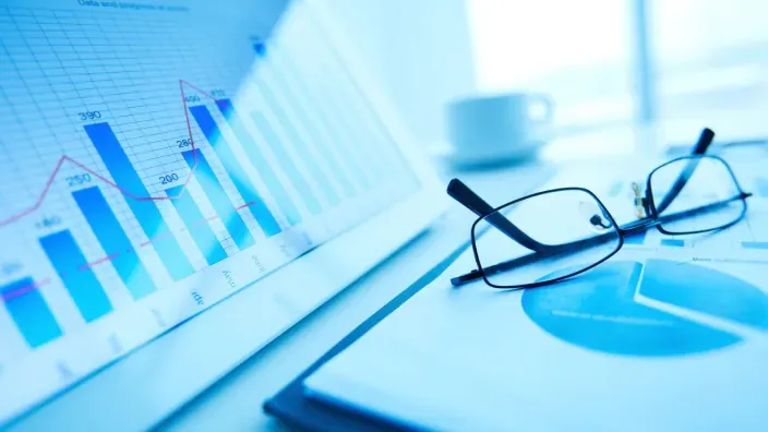 Gráficos financieros y de crecimiento impresos junto a unas gafas sobre una mesa de trabajo, representación de análisis económico.