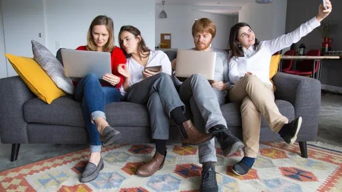 Grupo de amigos en el sofá usando portátiles, tablet y móvil conectados a la red WiFi doméstica.
