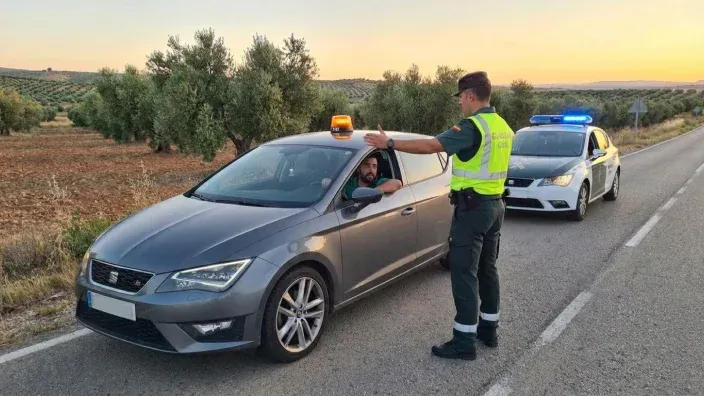 Conductor con chaleco reflectante colocando baliza V16 luminosa en el techo de su coche.