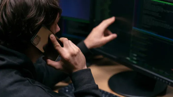 Ciberdelincuente realizando estafa telefónica o vishing frente a ordenadores tras el robo de datos.