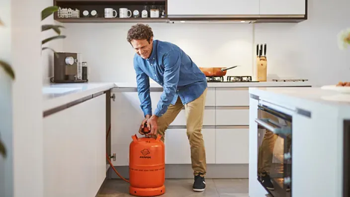 Hombre colocando una bombona de butano Repsol en la cocina junto al mueble bajo