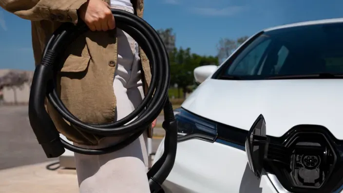 Persona sosteniendo el cable de carga junto a un coche eléctrico blanco estacionado.