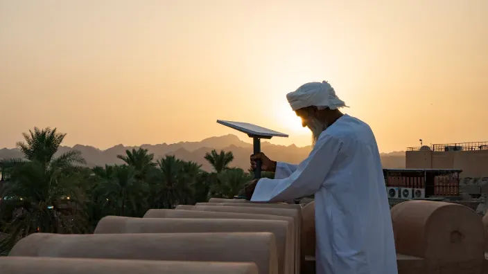 Hombre con vestimenta tradicional junto a una antena en una azotea al atardecer