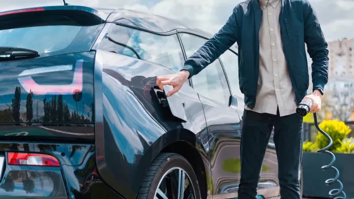 Hombre enchufando la manguera de carga en la toma de un coche eléctrico negro aparcado en la calle