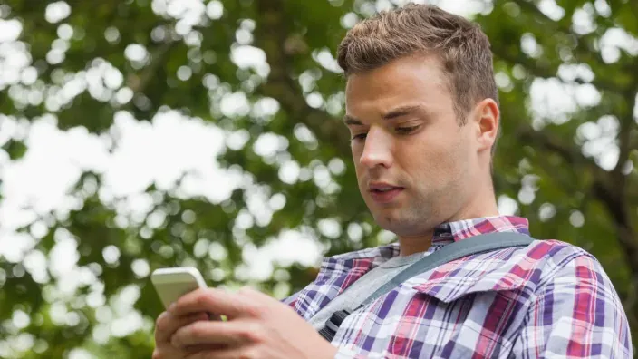 Joven usando su teléfono móvil al aire libre para representar la conectividad y el uso de datos en exteriores.