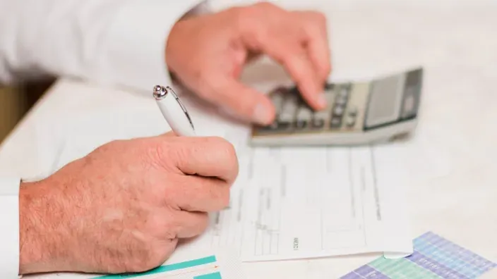 → Persona calculando y rellenando documentos fiscales con una calculadora.