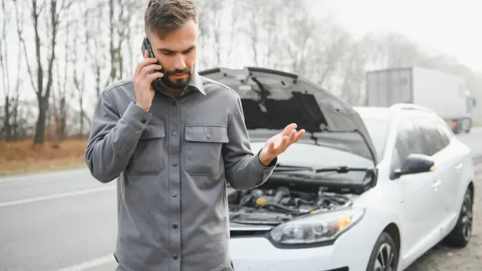 Hombre hablando por teléfono junto a un coche averiado con el capó abierto