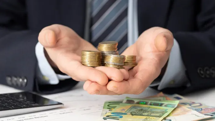Manos de un asesor con monedas y billetes de euro representando la rentabilidad y gestión de ahorros e inversiones.