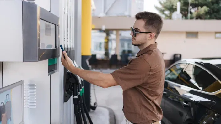 Hombre junto a un surtidor de gasolina pulsando la pantalla de pago