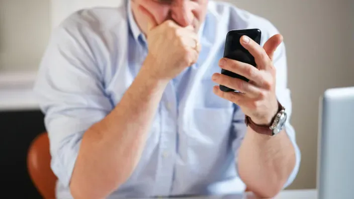 Hombre preocupado consultando su smartphone por una posible incidencia financiera o factura elevada.