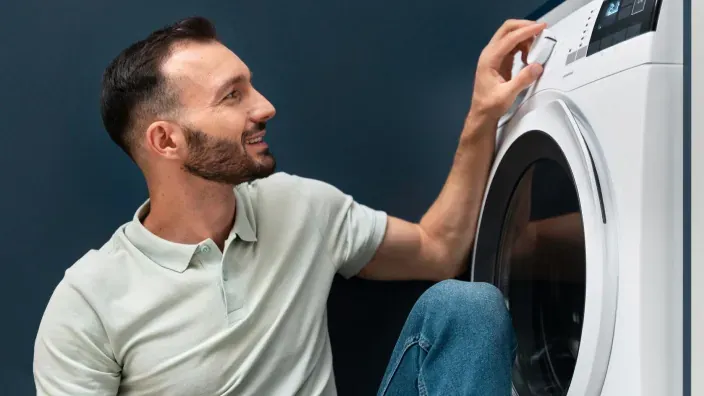Hombre ajustando el panel de control de una lavadora moderna en casa.