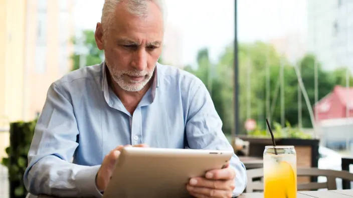 Hombre mayor usando una tablet en una terraza. Vida conectada y ocio digital para personas de la tercera edad.