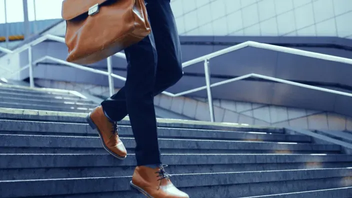 Hombre vestido de traje descendiendo unas escaleras con un maletín de cuero en la mano.