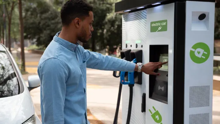 Hombre usando la pantalla de un punto de recarga para coche eléctrico