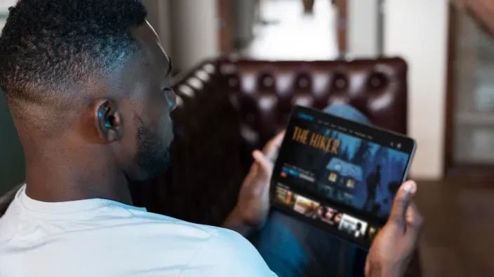 Hombre viendo una película en su tablet en casa, utilizando una plataforma de streaming de vídeo.