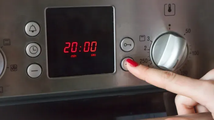 Persona ajustando el temporizador de un horno eléctrico con pantalla digital.