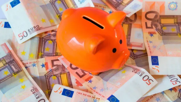 Hucha de cerdo naranja sobre billetes de 50 euros.