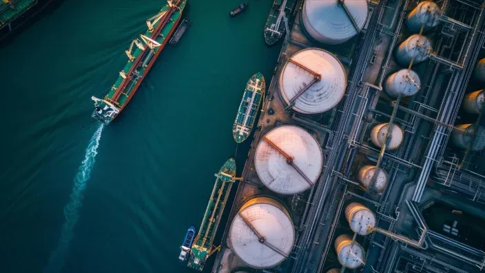 Vista aérea de un puerto comercial con buques de carga y tanques de almacenamiento de combustible para el sector energético.