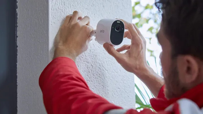 Técnico instalando una cámara de seguridad Arlo en la pared exterior de una vivienda.