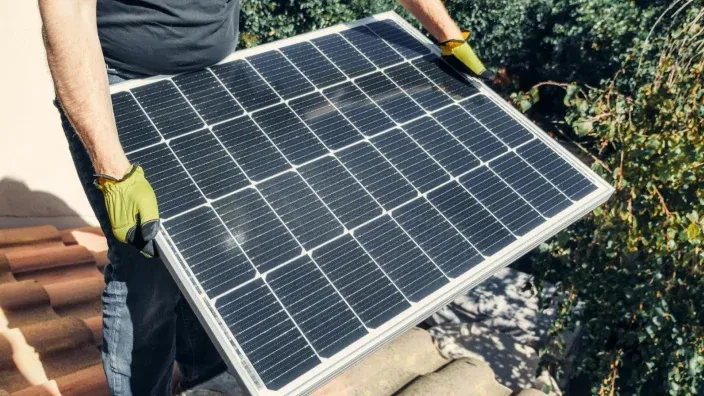 Persona instalando un panel solar en el tejado de una vivienda para aprovechar la energía solar y fomentar el autoconsumo.