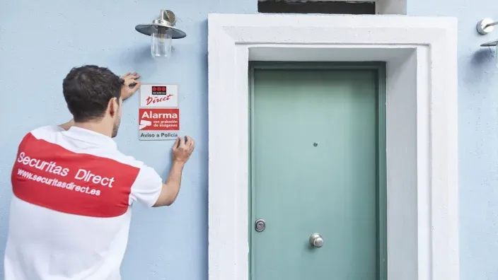 Técnico de Securitas Direct instalando la placa disuasoria de la alarma en la fachada de una casa. Seguridad y protección del hogar.