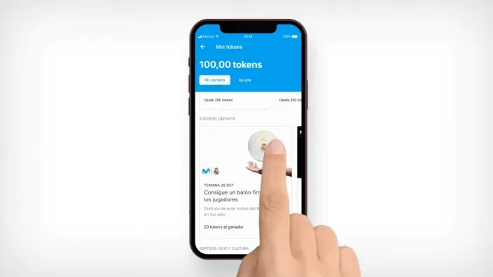Mano sosteniendo un móvil con la app de Tokens de Movistar, el programa de fidelización para clientes de la operadora.