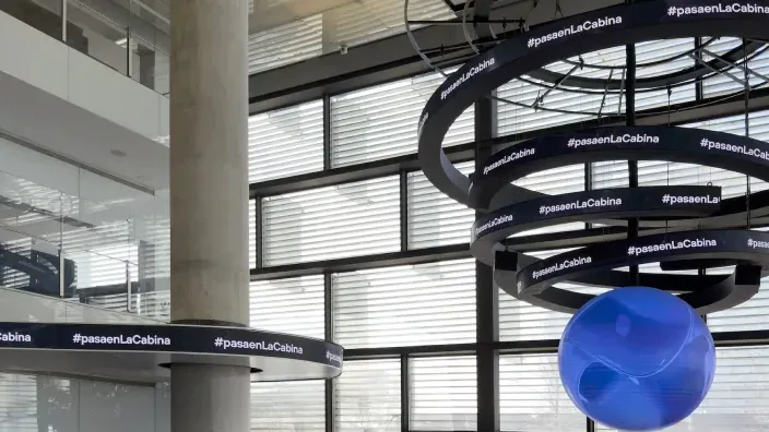 Interior de un edificio con estructuras circulares colgantes y el texto paseaenLaCabina