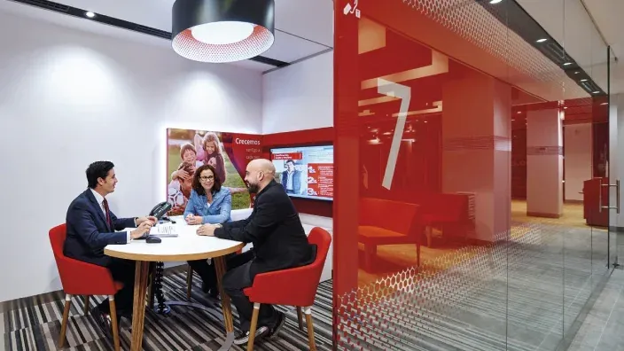 Interior moderno de una oficina del Banco Santander, con clientes atendidos en una mesa.