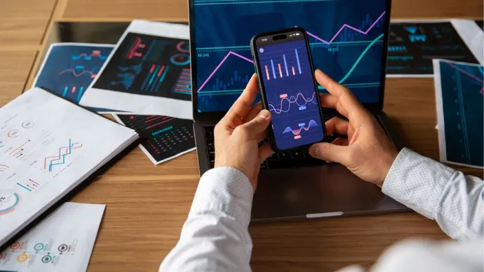 Persona revisando gráficos financieros en su portátil y teléfono móvil, representando la gestión digital de inversiones.