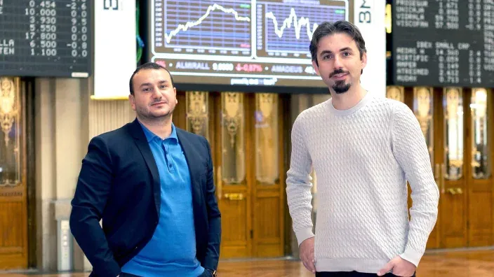 Andrei Manuel y Leif Ferreira, fundadores de Bit2Me, posan en la Bolsa de Madrid ante paneles de cotización bursátil.
