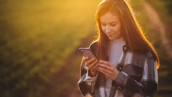 Mujer consultando su móvil al aire libre bajo la luz del atardecer para representar la conectividad en exteriores.