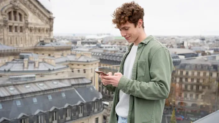 Joven turista usando el móvil con roaming en una azotea con vistas a París.