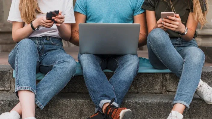 Estudiantes jóvenes sentados en escaleras usando portátiles y móviles para estudiar o navegar.