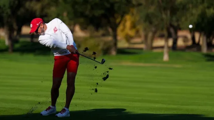 Jugador de golf realizando un golpe sobre el césped de un campo durante un torneo.