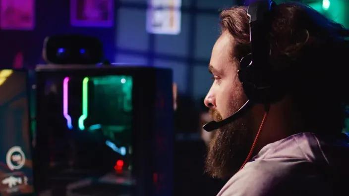 Perfil de un gamer con barba y auriculares, concentrado en un videojuego en su PC con luces RGB. eSports y streaming.