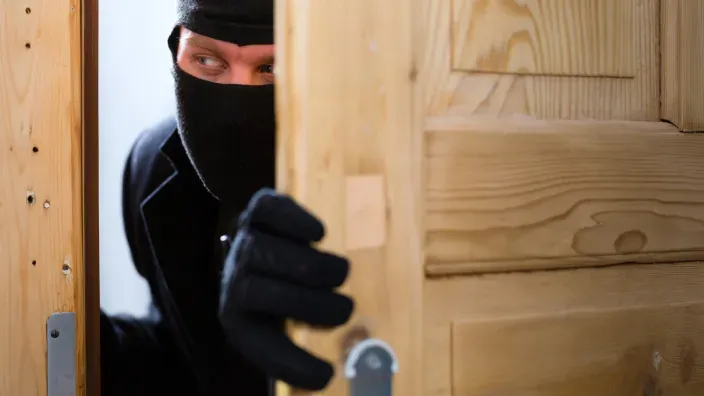 Ladrón encapuchado intentando forzar la puerta de madera de una vivienda durante un robo