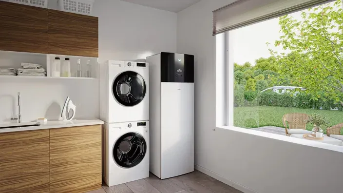 Lavadero con una lavadora, una secadora y un equipo de aerotermia junto a una ventana