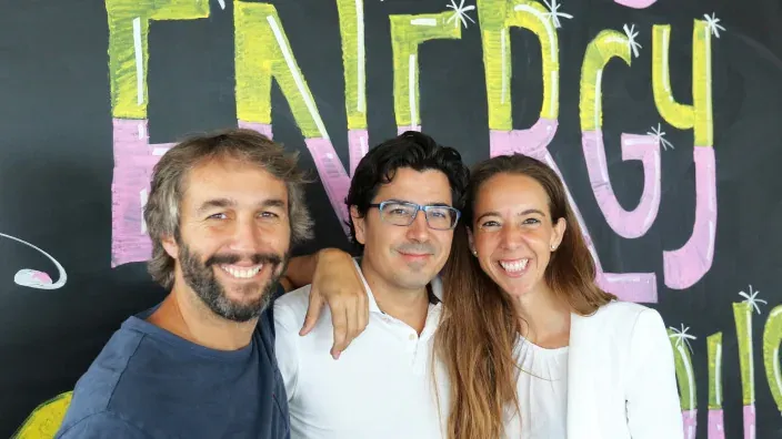 Los tres fundadores de Holaluz posando y sonriendo frente a un mural con el nombre de Holaluz