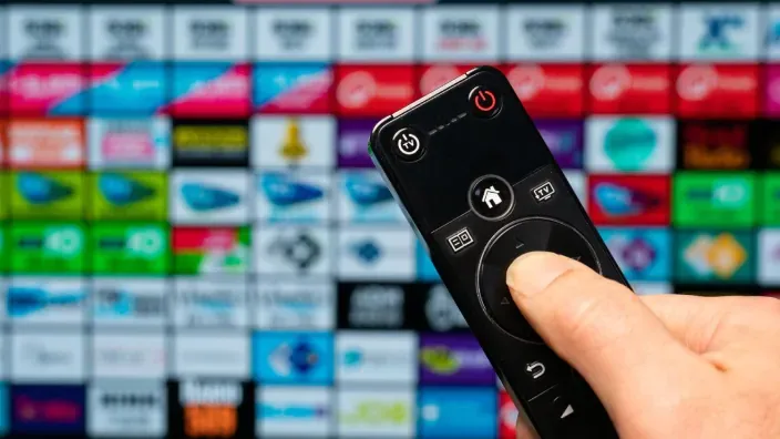Mano con mando a distancia frente a una Smart TV con variedad de canales y aplicaciones de streaming.