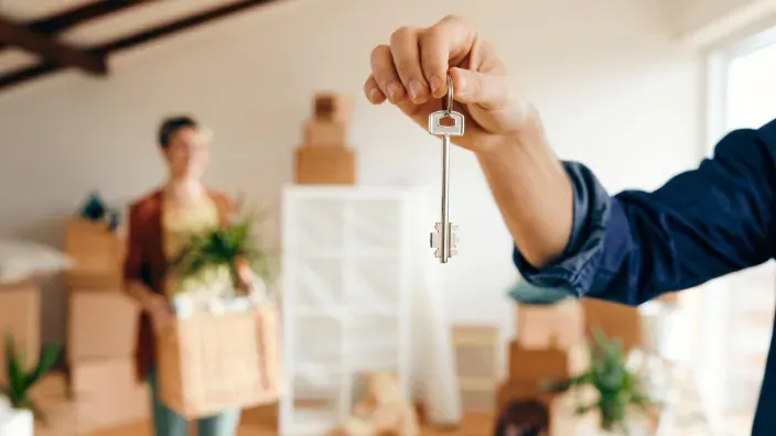 Mano sosteniendo unas llaves de vivienda con una persona y cajas al fondo