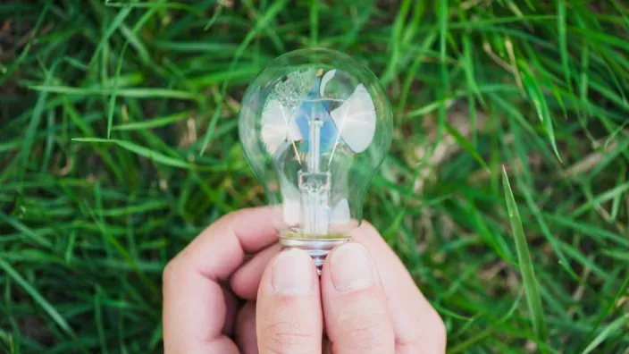 Mano sosteniendo una bombilla transparente sobre césped