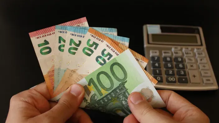 Manos sosteniendo varios billetes de euro junto a una calculadora