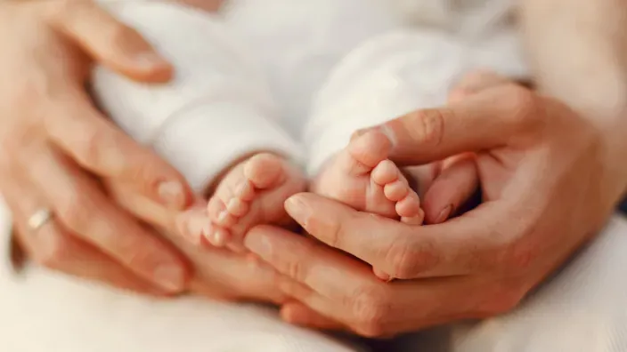Primer plano de unas manos adultas sosteniendo los pies de un bebé.