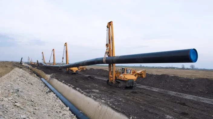 Construcción de gasoducto con maquinaria pesada colocando tubería en zanja.