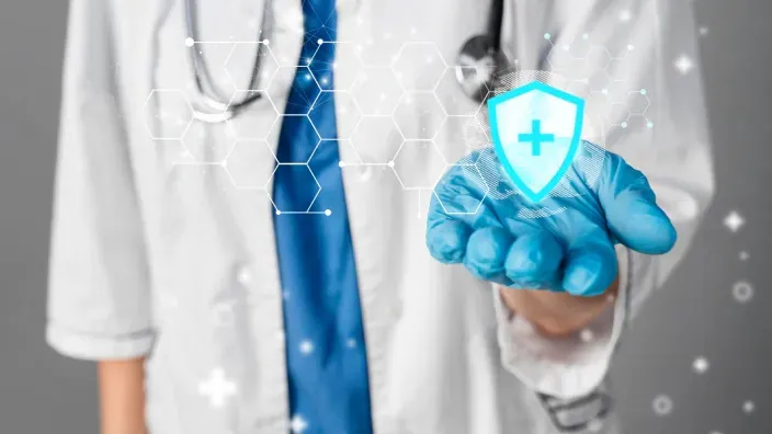 Médico con bata y guante sosteniendo un escudo digital con una cruz sanitaria