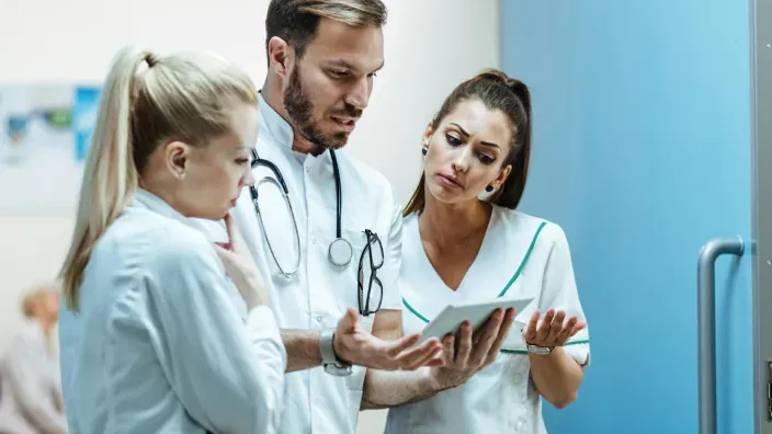 Equipo de profesionales sanitarios conversando mientras consultan información en una tablet dentro de un centro médico.