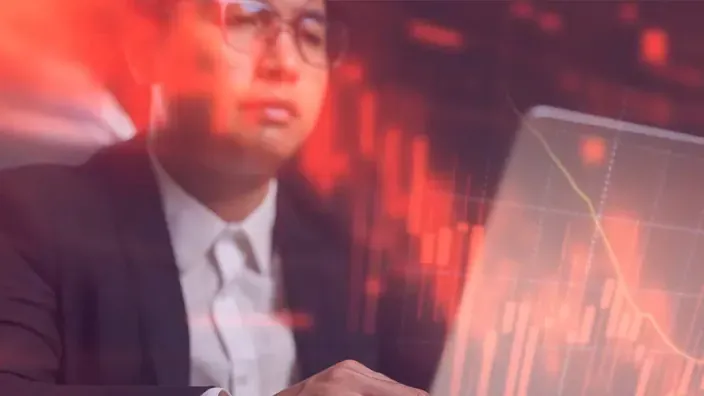 Inversor analizando gráficos bursátiles en rojo con tendencia bajista, representando pérdidas financieras.