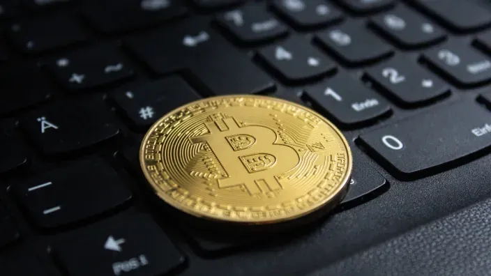 Moneda física de la criptomoneda Bitcoin sobre el teclado de un ordenador portátil, representando la inversión digital.