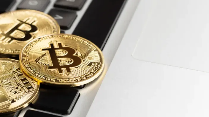 Monedas físicas de la criptomoneda Bitcoin sobre un ordenador portátil, representando la inversión en activos digitales.